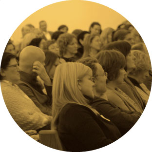 A large group of adults sitting in a room, engaged and focused on listening to somebody speaking to them.