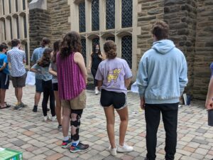 A photograph of a group of teens who are all facing an adult instructing them.